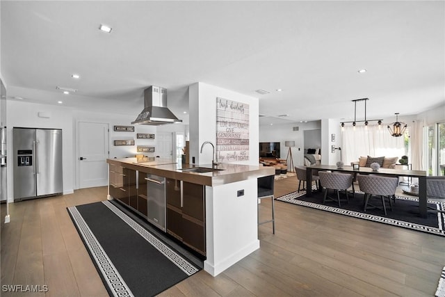 kitchen with sink, island range hood, light wood-type flooring, stainless steel fridge, and an island with sink