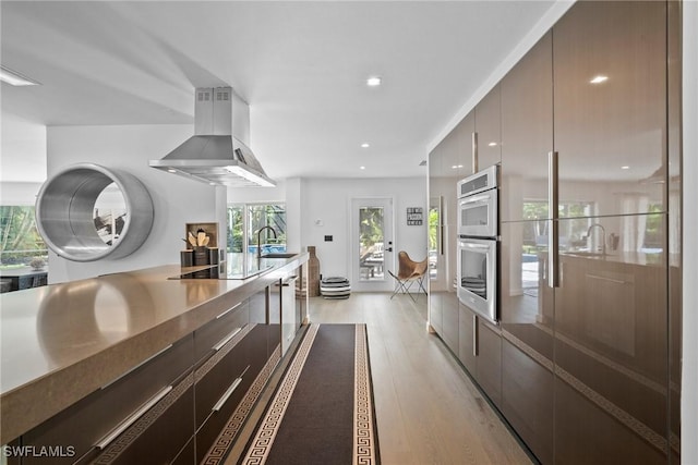 kitchen featuring sink, light hardwood / wood-style flooring, black electric cooktop, double oven, and island exhaust hood