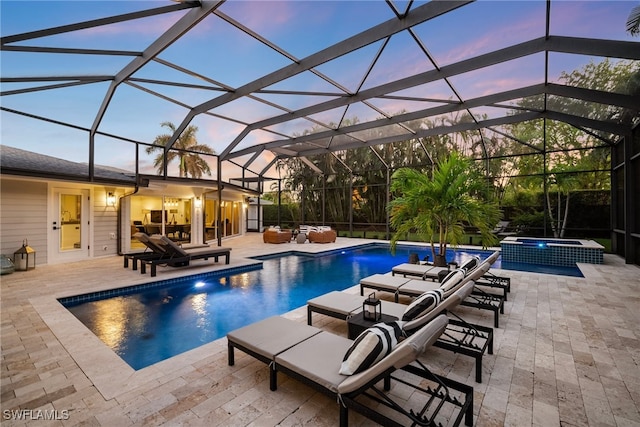 pool at dusk with glass enclosure, an in ground hot tub, and a patio area