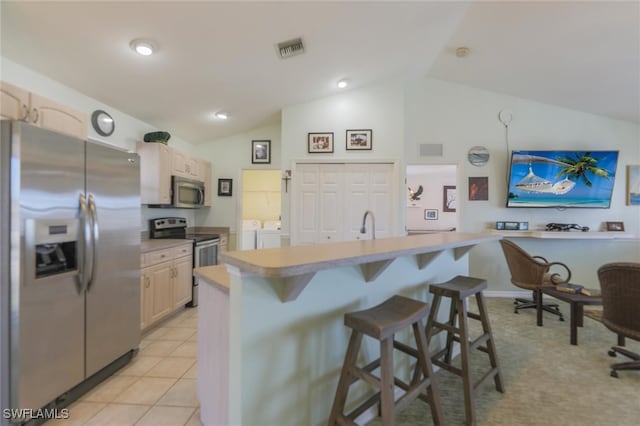 kitchen featuring a kitchen breakfast bar, stainless steel appliances, washer and dryer, light tile patterned floors, and lofted ceiling