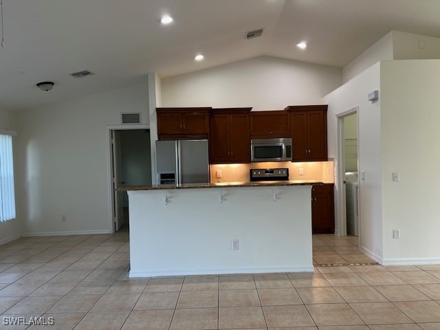 kitchen with appliances with stainless steel finishes, vaulted ceiling, light tile patterned floors, and a center island with sink