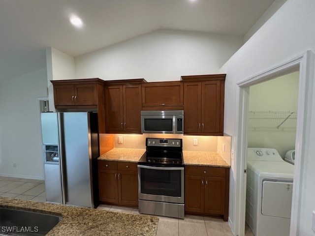 kitchen with stainless steel appliances, washer and clothes dryer, light stone counters, and vaulted ceiling