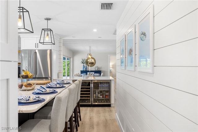 kitchen with stainless steel refrigerator, white cabinetry, hanging light fixtures, and light hardwood / wood-style floors