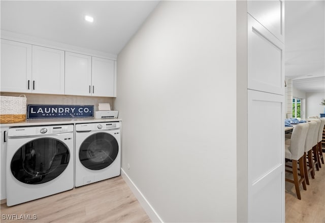 laundry room featuring washer and dryer, light hardwood / wood-style flooring, and cabinets