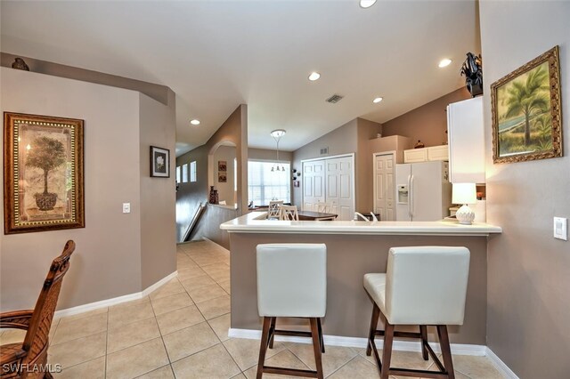 kitchen featuring a kitchen bar, kitchen peninsula, white fridge with ice dispenser, and vaulted ceiling