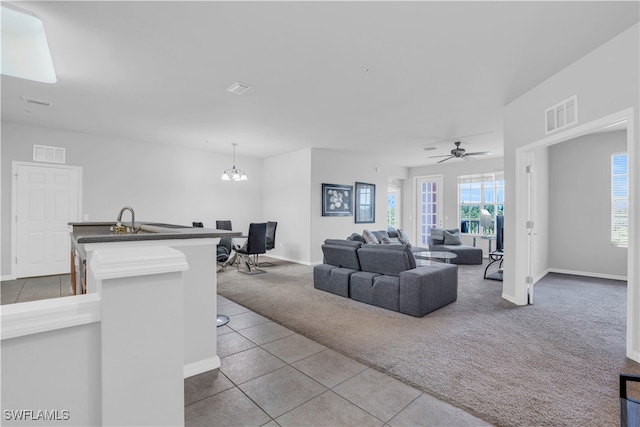 living room with ceiling fan with notable chandelier, plenty of natural light, sink, and carpet