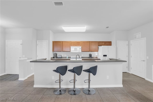 kitchen with a kitchen bar, light tile patterned floors, sink, an island with sink, and white appliances