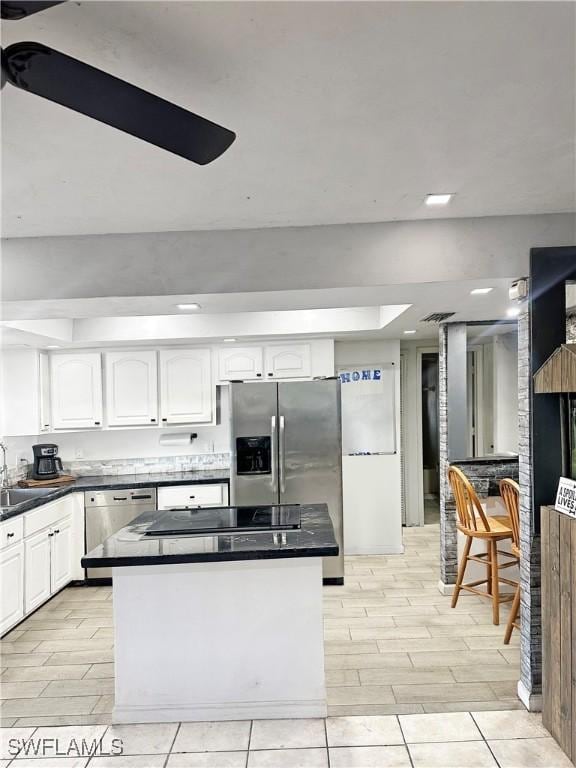 kitchen featuring dark countertops, white cabinets, stainless steel appliances, and a center island