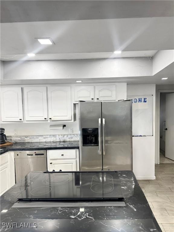 kitchen with stainless steel refrigerator with ice dispenser, dark stone countertops, cooktop, white cabinets, and dishwashing machine