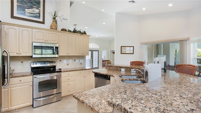 kitchen with stainless steel appliances, light stone countertops, sink, and high vaulted ceiling