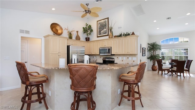 kitchen featuring stainless steel appliances, a breakfast bar area, ceiling fan, and light stone countertops