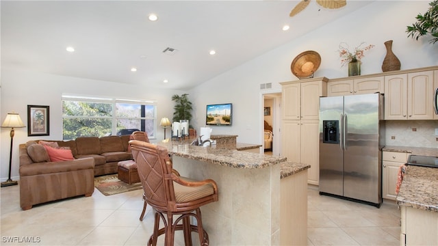 kitchen with tasteful backsplash, light stone counters, stainless steel fridge, vaulted ceiling, and cream cabinetry