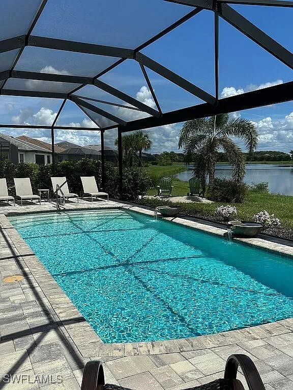 view of pool featuring a patio, pool water feature, glass enclosure, and a water view