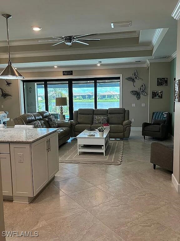 living room featuring ceiling fan, ornamental molding, and a raised ceiling