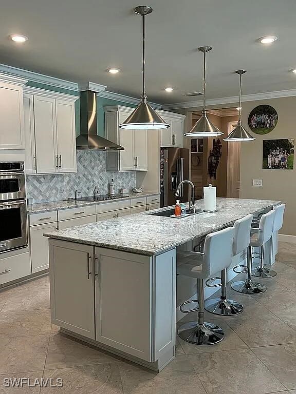 kitchen with white cabinets, decorative light fixtures, wall chimney exhaust hood, and a spacious island