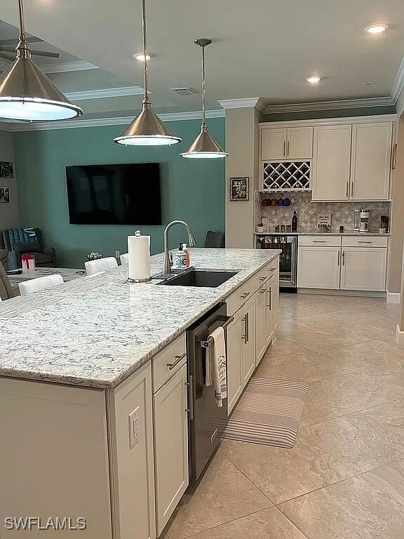 kitchen featuring pendant lighting, sink, crown molding, light stone countertops, and a center island with sink