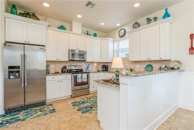 kitchen with kitchen peninsula, light stone countertops, tasteful backsplash, stainless steel appliances, and white cabinetry