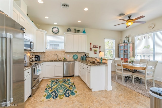 kitchen featuring kitchen peninsula, stainless steel appliances, white cabinetry, and dark stone countertops