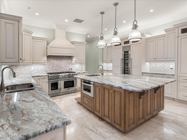 kitchen with custom exhaust hood, stainless steel appliances, sink, a large island with sink, and decorative light fixtures