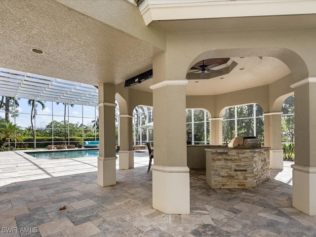 view of patio / terrace featuring glass enclosure, ceiling fan, and exterior kitchen