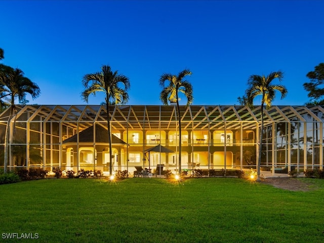 back house at dusk featuring a lawn and a lanai