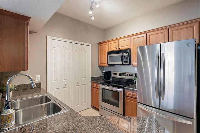 kitchen featuring light tile patterned floors, brown cabinetry, dark countertops, stainless steel appliances, and a sink