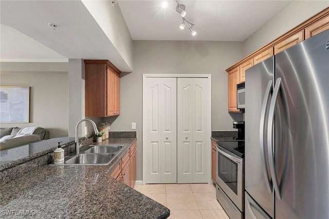 kitchen with light tile patterned floors, stainless steel appliances, open floor plan, a sink, and dark stone countertops