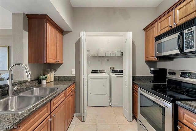 kitchen with brown cabinetry, independent washer and dryer, stainless steel electric range, a sink, and light tile patterned flooring