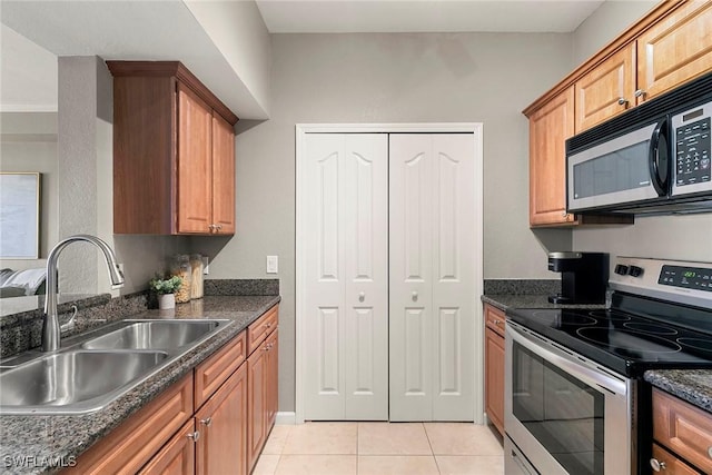 kitchen featuring black microwave, light tile patterned flooring, a sink, dark stone countertops, and stainless steel range with electric stovetop