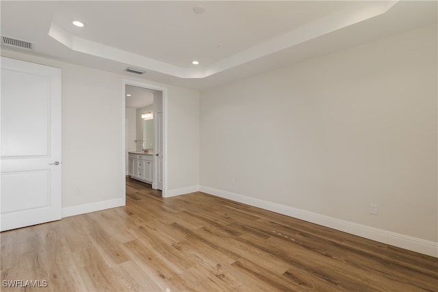 unfurnished bedroom with a raised ceiling, connected bathroom, and light wood-type flooring