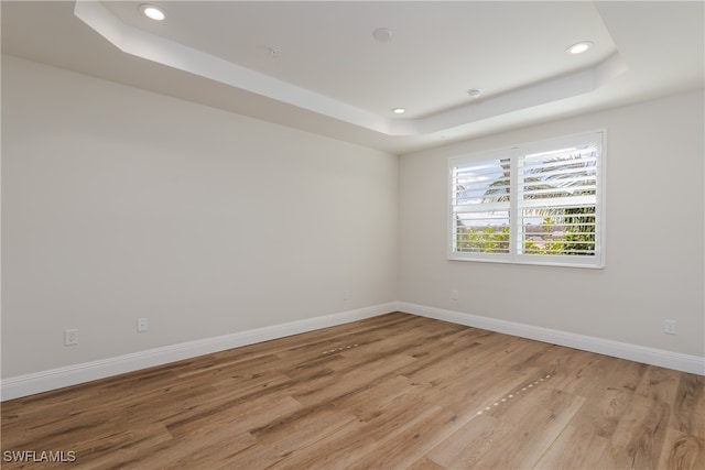 spare room with a raised ceiling and light hardwood / wood-style flooring