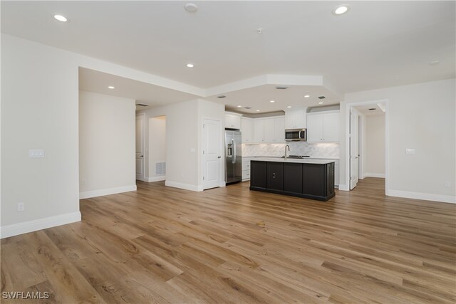 kitchen with white cabinetry, stainless steel appliances, tasteful backsplash, a center island with sink, and light wood-type flooring