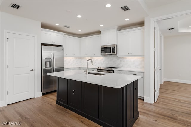 kitchen with a center island with sink, sink, light hardwood / wood-style floors, white cabinetry, and stainless steel appliances