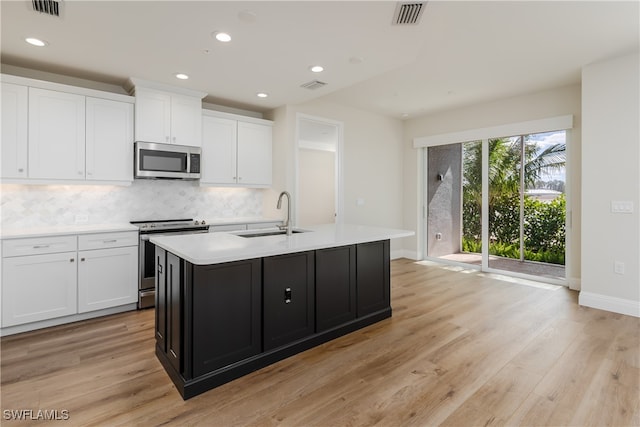 kitchen featuring a center island with sink, white cabinets, sink, light hardwood / wood-style flooring, and appliances with stainless steel finishes