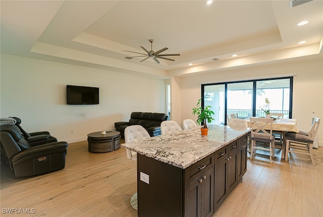 kitchen with a kitchen bar, light wood-type flooring, dark brown cabinets, and a raised ceiling