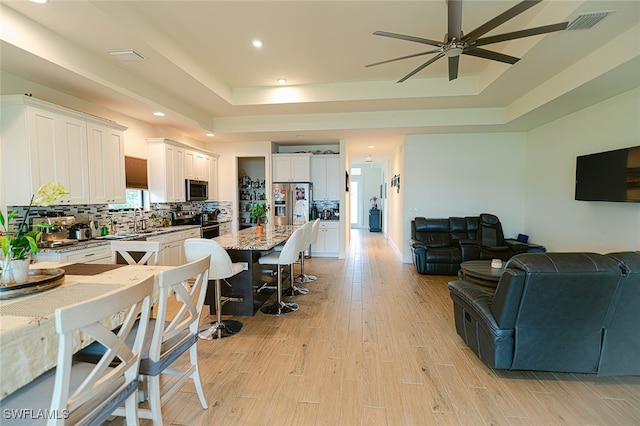 kitchen featuring light hardwood / wood-style flooring, tasteful backsplash, a breakfast bar, white cabinetry, and appliances with stainless steel finishes