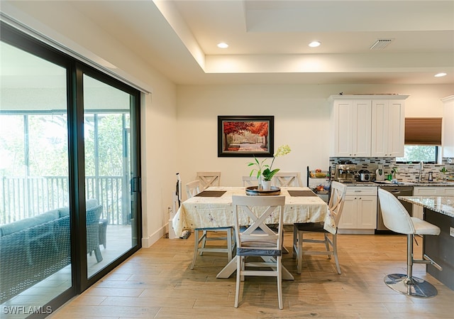 dining room with sink, light wood-type flooring, and a raised ceiling