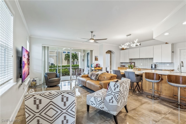 tiled living room with crown molding, sink, and ceiling fan with notable chandelier