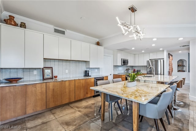 kitchen featuring a large island, crown molding, pendant lighting, white cabinets, and appliances with stainless steel finishes