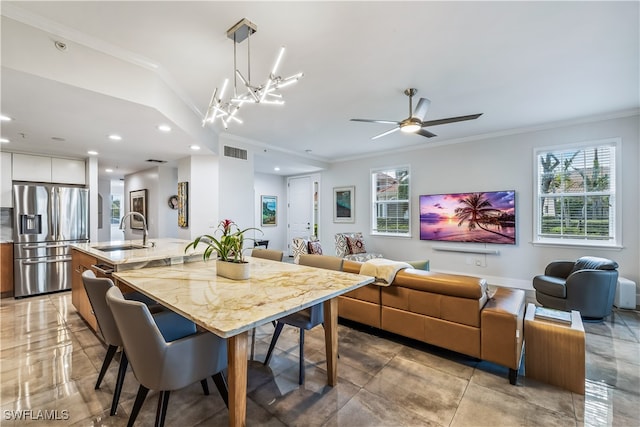 dining space with ceiling fan with notable chandelier, ornamental molding, and sink