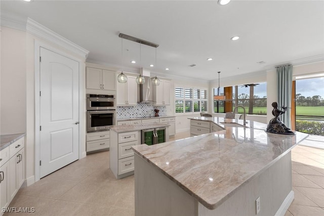 kitchen featuring a large island, stainless steel double oven, wall chimney range hood, and a sink