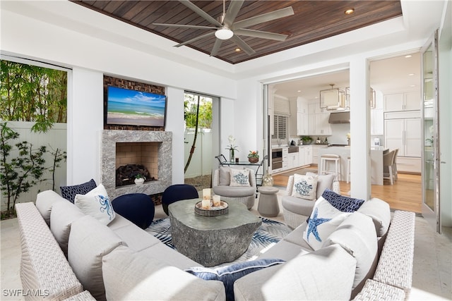 living room with a high end fireplace, a tray ceiling, ceiling fan, and wood ceiling