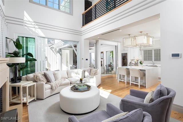 living room with a towering ceiling, light wood-type flooring, an inviting chandelier, and a wealth of natural light