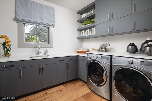 laundry area featuring washing machine and dryer, cabinets, sink, and light hardwood / wood-style floors