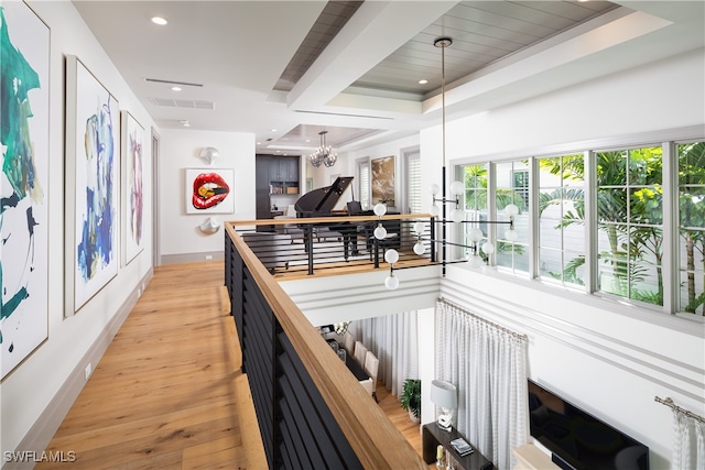 corridor with a raised ceiling, light hardwood / wood-style flooring, and an inviting chandelier