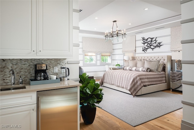 bedroom featuring a raised ceiling, light hardwood / wood-style flooring, an inviting chandelier, and sink