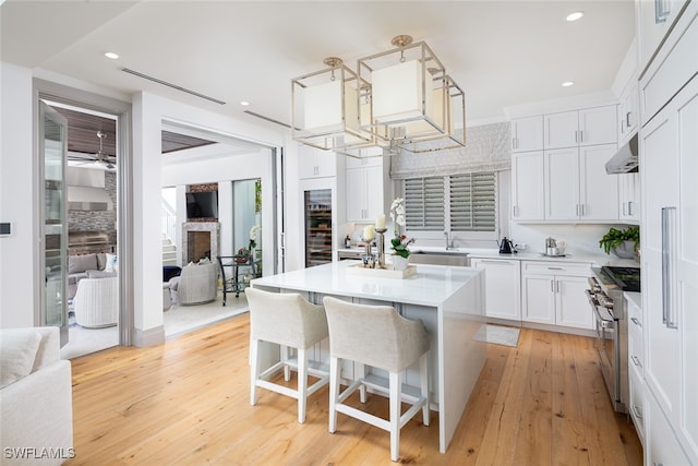 kitchen with high end range, a breakfast bar, a kitchen island, light hardwood / wood-style floors, and white cabinetry