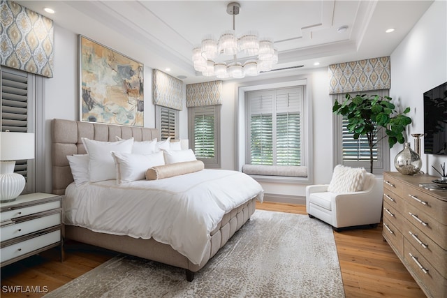 bedroom with a chandelier, a tray ceiling, and light hardwood / wood-style flooring