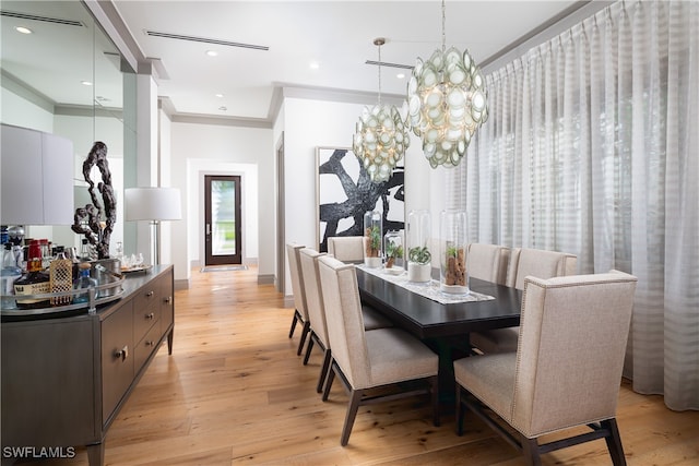 dining area with a notable chandelier, light wood-type flooring, and ornamental molding