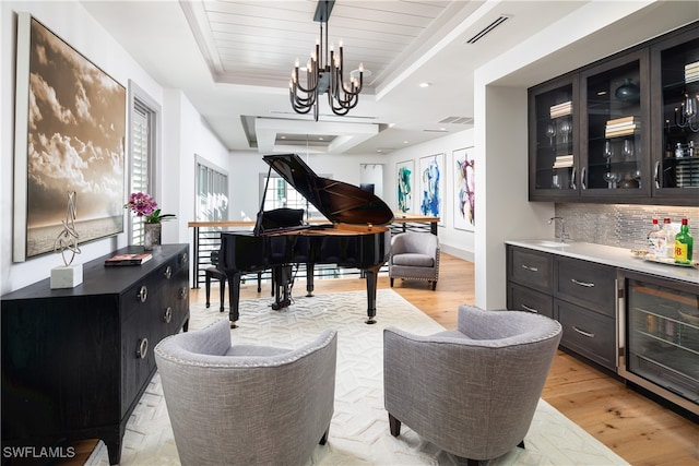 misc room featuring wet bar, light hardwood / wood-style flooring, a tray ceiling, beverage cooler, and a chandelier